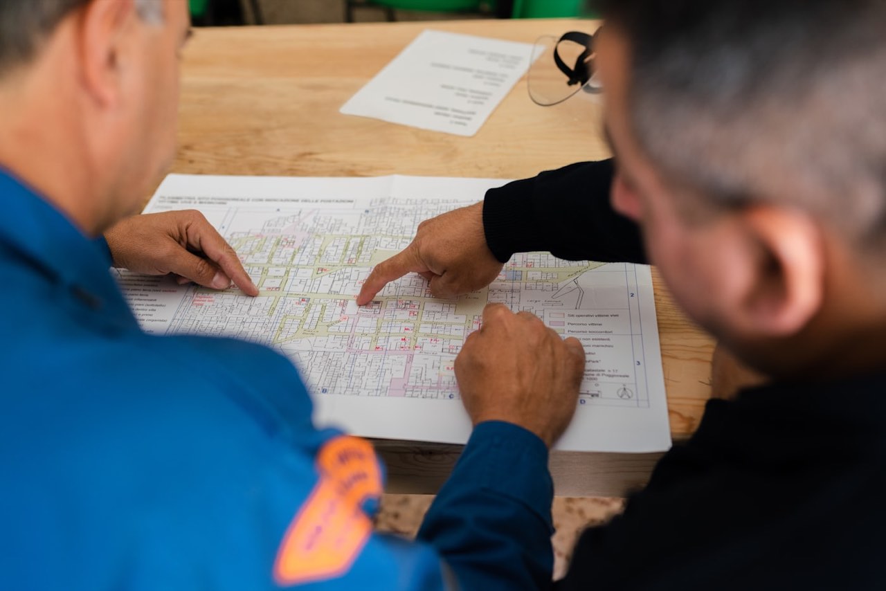 Two people leaning over a printed site drawing on a table, pointing at the same detail